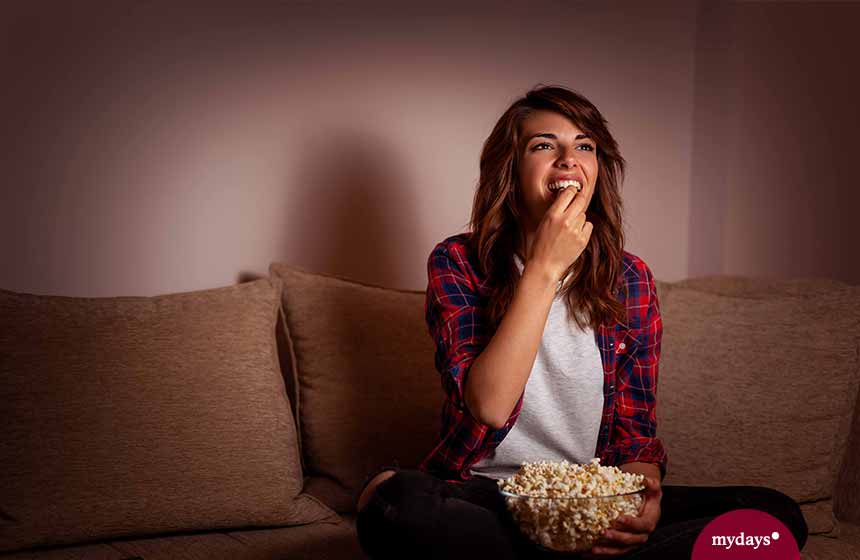 Frau isst Snacks vor dem Fernseher, Popcorn