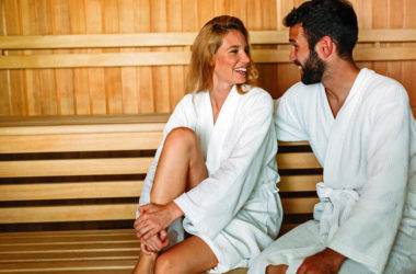 Mann und Frau im Bademantel sitzen in der Sauna und lächeln sich an