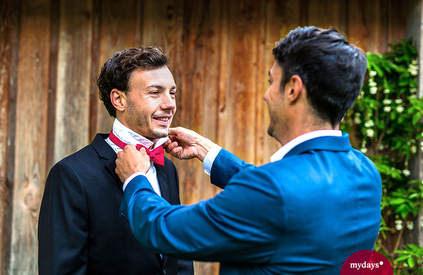 Trauzeuge hilft Bräutigam beim Anziehen.