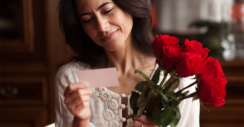 Frau freut sich über rote Rosen und einen Liebesbrief
