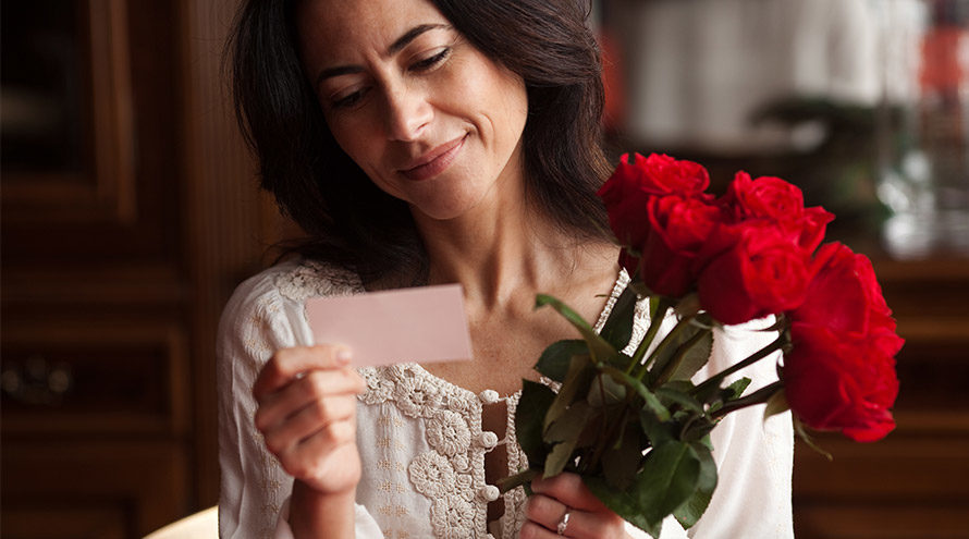 Frau freut sich über rote Rosen und einen Liebesbrief